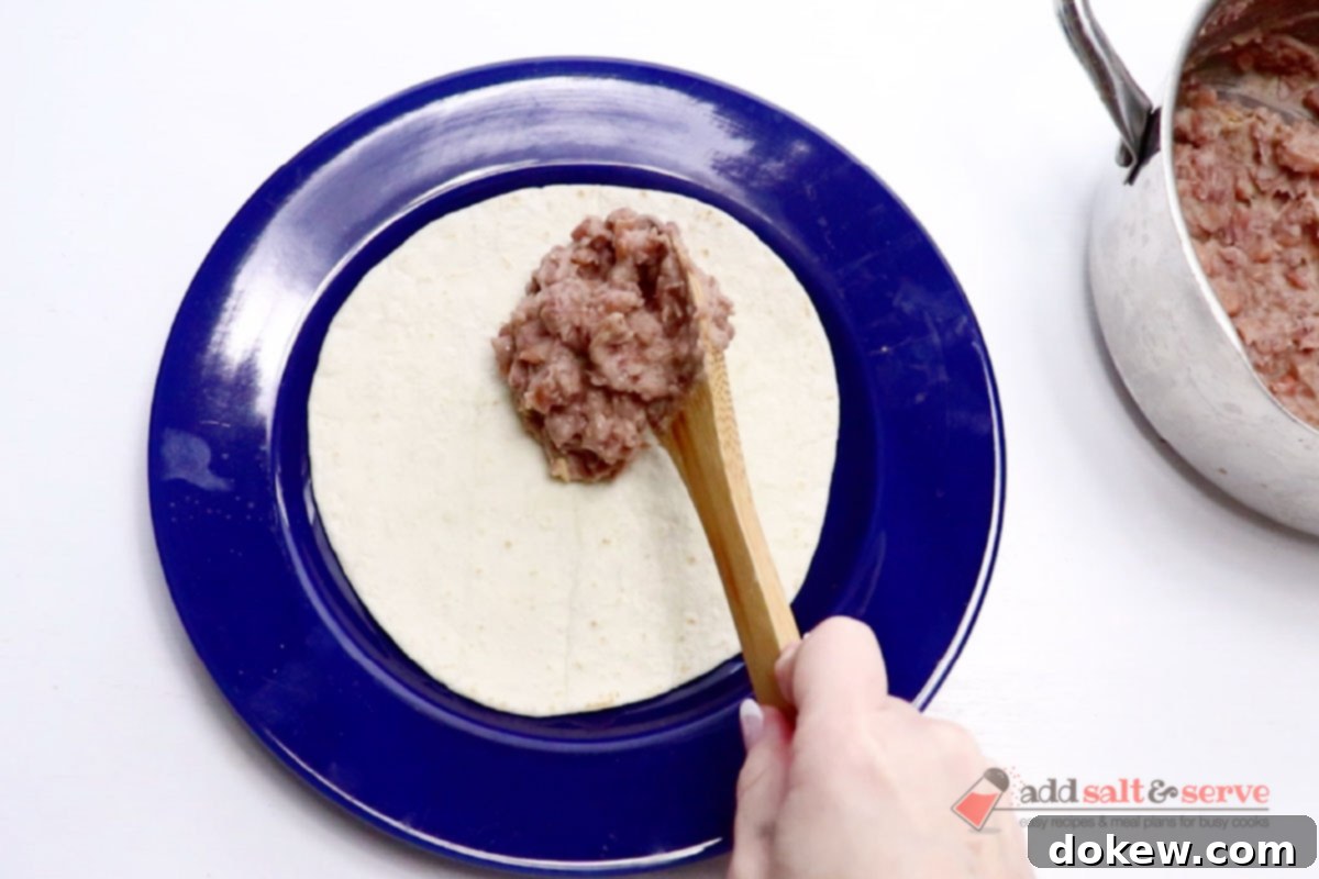 A tortilla on a plate with a spoonful of bean burrito filling being placed onto its center.