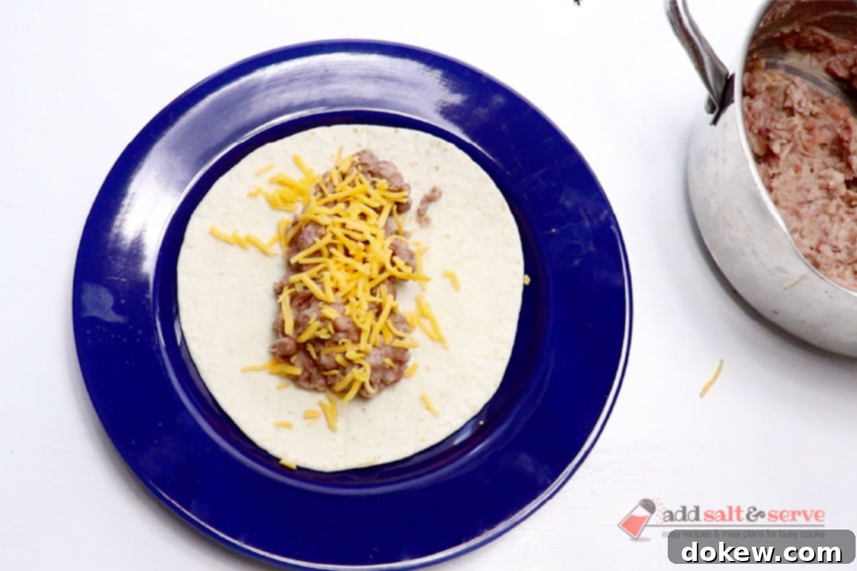A tortilla with bean burrito filling and shredded cheddar cheese before folding into a burrito.