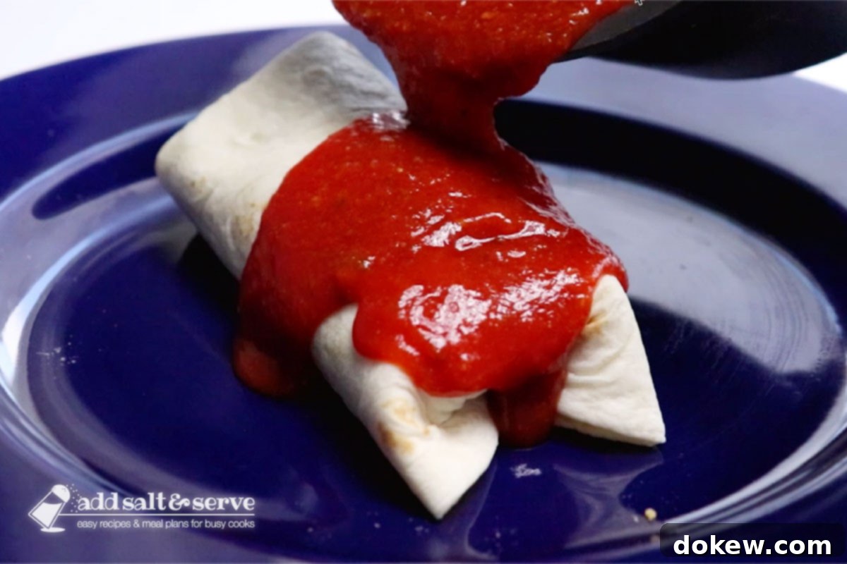 A burrito on a plate with homemade mojado sauce being poured generously over it.
