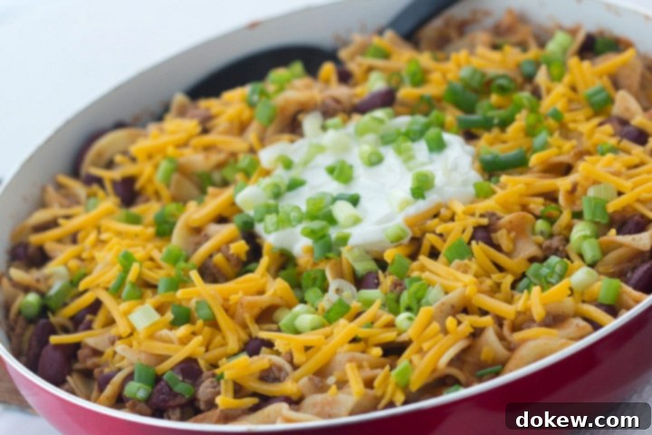 Southwestern Hamburger Skillet A vibrant Southwestern Ground Beef Skillet featuring tender kidney beans, seasoned ground beef, and soft egg noodles, generously topped with shredded cheddar cheese, a dollop of creamy sour cream, and a sprinkle of fresh chopped green onions. The dish is presented in a rustic cast-iron skillet, ready to serve.