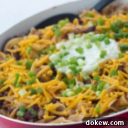 Southwestern Ground Beef Skillet 2 Kidney beans, ground beef, and egg noodles topped with shredded cheddar cheese, sour cream, and chopped green onions, in a skillet.