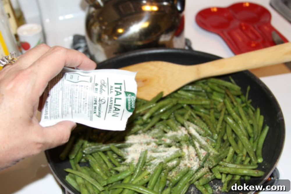 Green Beans Seasoned with Italian Dressing Sautéed green beans in a black fry pan with Good Seasons Italian dressing mix being added