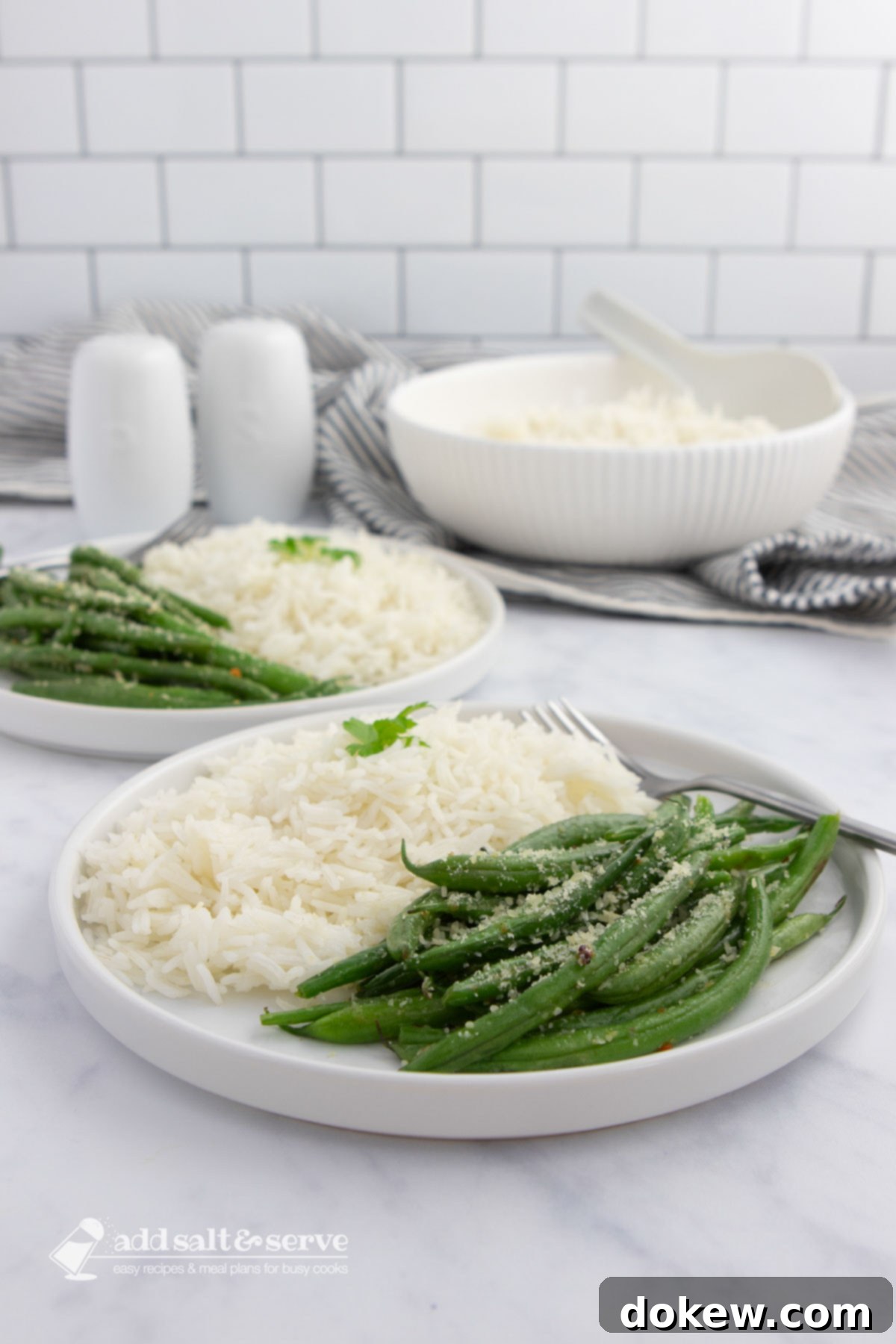 Savory Green Beans 3 Seasoned green beans garnished with Parmesan cheese on plates with white rice with a serving bowl of rice in the background.