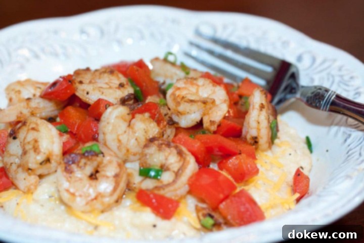 Classic Shrimp and Grits Shrimp, diced tomatoes, and shredded cheddar cheese on grits, on a white plate with a fork, ready to be served.