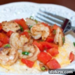 Southern Comfort: Shrimp and Grits 2 Shrimp, diced tomatoes, and shredded cheddar cheese on grits, on a white plate with a fork.