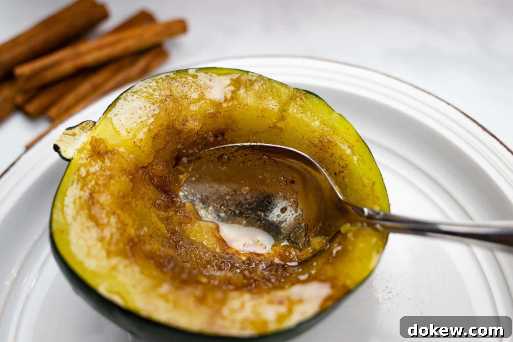 A beautifully prepared plate of microwave acorn squash, glistening with melted butter, golden brown sugar, and a sprinkle of warm cinnamon. A spoon rests beside it, ready to scoop out the tender, sweet flesh.