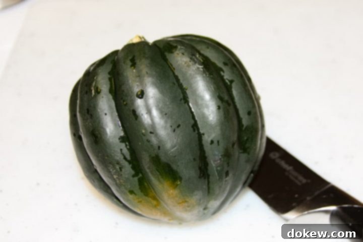 easy-microwave-acorn-squash-ip-6 copy-min A whole, deep green acorn squash placed on a wooden cutting board, with a large chef's knife beside it, illustrating the start of the preparation process.