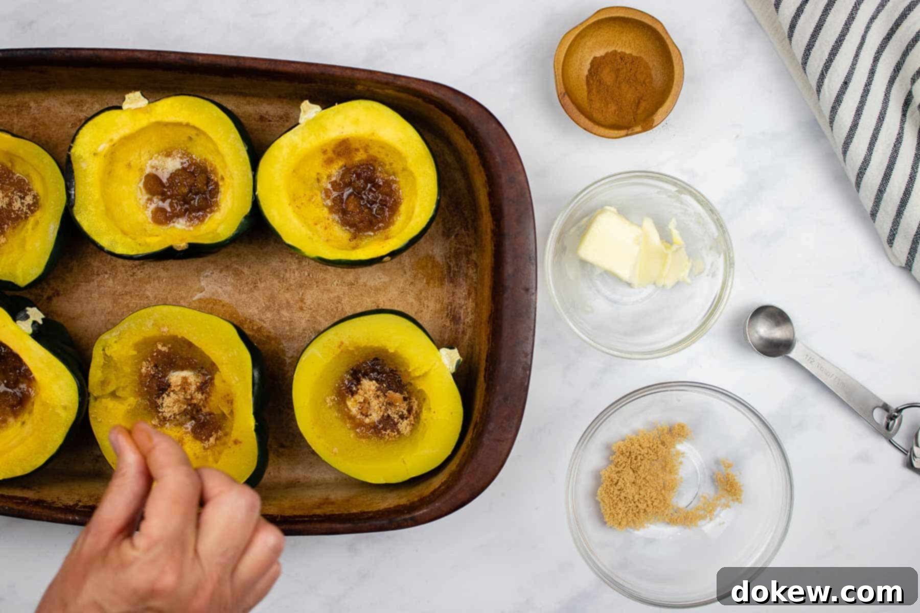 Quick and Easy Microwave Acorn Squash 6 A hand sprinkling ground cinnamon over cooked acorn squash halves, which are already topped with melting butter and brown sugar, enhancing their sweet aroma.