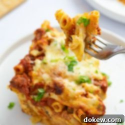 Classic Cheesy Meatless Baked Ziti 11 A fork lifts a bite of Cheesy Meatless Baked Ziti, garnished with fresh parsley, above a full plate of the dish.