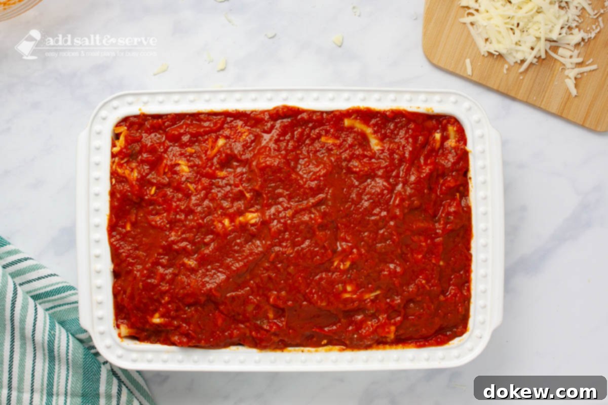 Classic Cheesy Meatless Baked Ziti 6 A baking pan filled with layers of baked ziti, showing the final layer of reserved marinara sauce spread smoothly over the pasta and cheese.