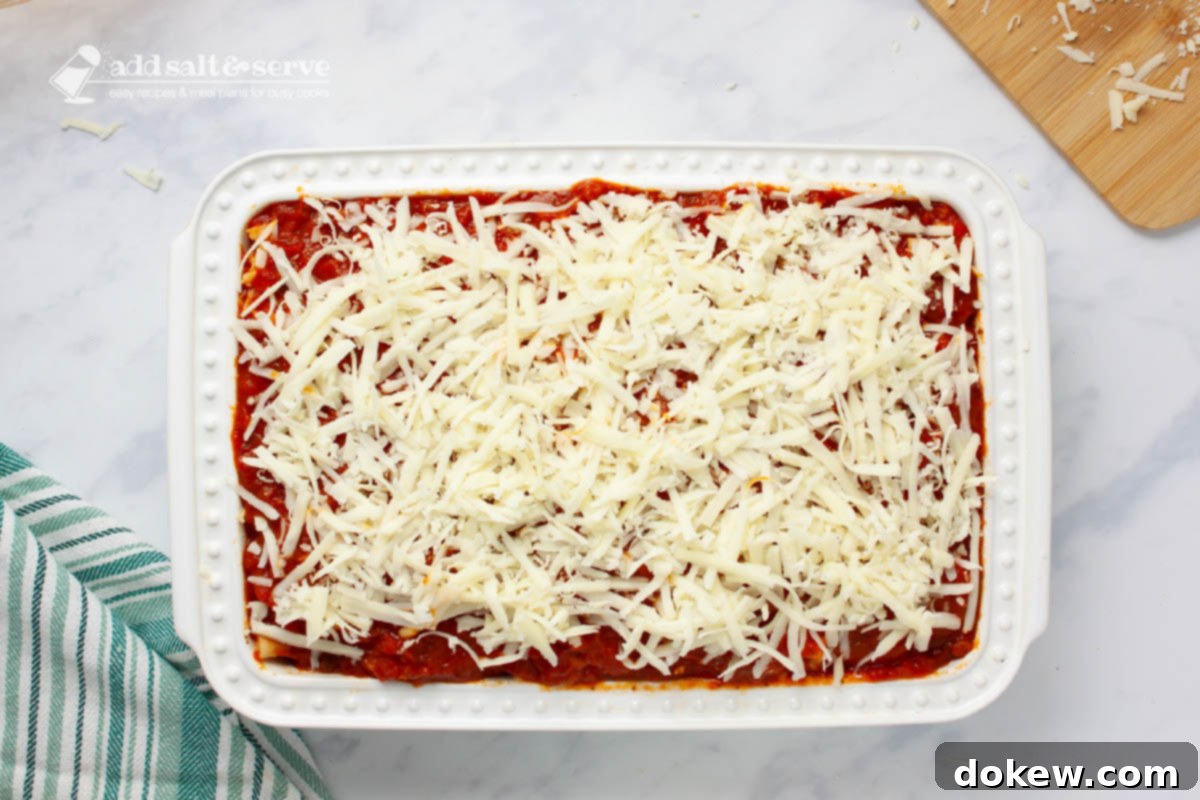 Classic Cheesy Meatless Baked Ziti 7 A baking pan showing the final layer of mozzarella cheese generously sprinkled over the marinara sauce and pasta layers, ready for baking.