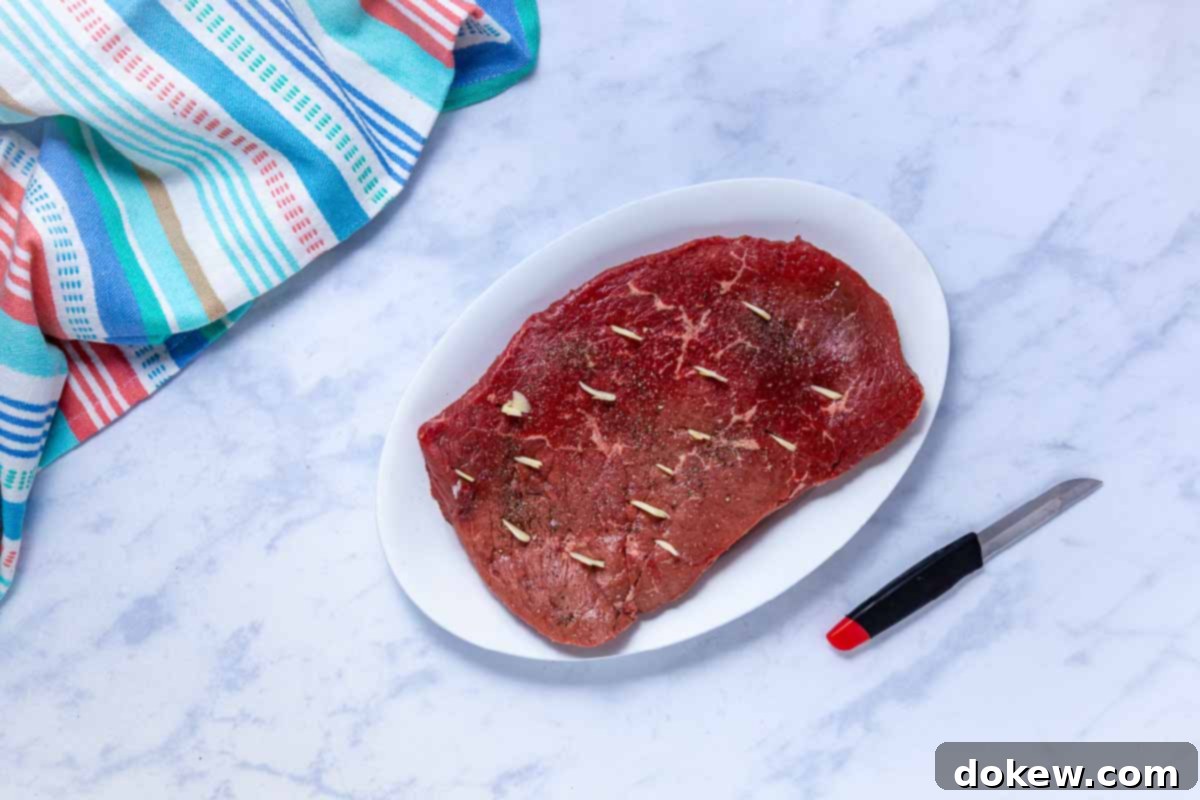 Tender Slow Cooker London Broil in Savory Au Jus 5 Uncooked London broil roast seasoned with salt and pepper with sliced garlic in slits cut into the roast.