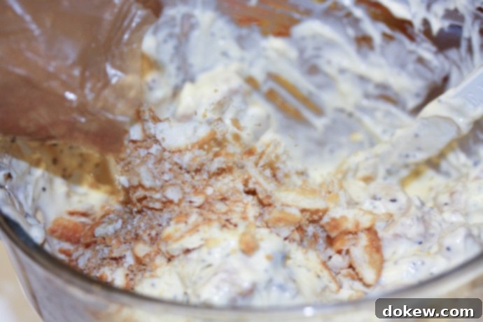 Creamy Poppy Seed Chicken Casserole Assembly - Chicken with crackers Creamy Poppy Seed Chicken Casserole Assembly - Cooked chicken with sour cream, soup, poppy seeds, and crushed crackers mixed together.