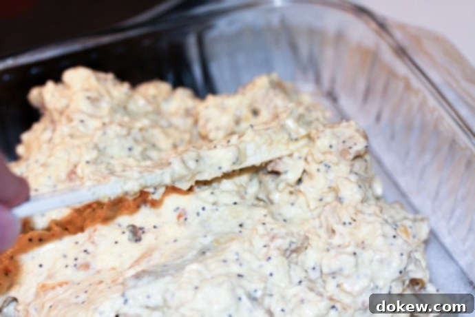 Spreading poppy seed chicken mixture in pan Spreading the poppy seed chicken mixture evenly into a 9x13 inch baking pan.