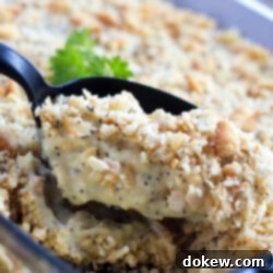 Creamy Poppy Seed Chicken Casserole 2 A black spoon is scooping Poppy Seed Chicken Casserole out of a clear glass casserole dish.