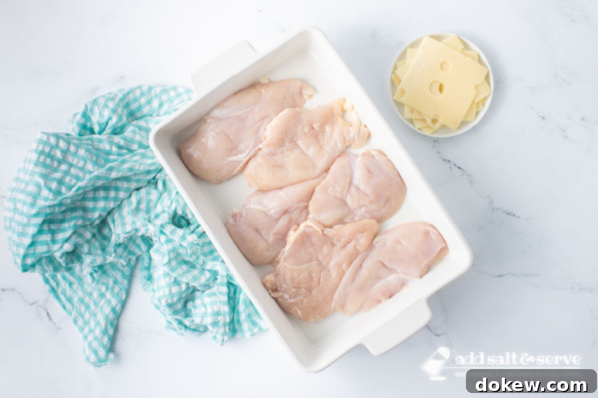 Savory White Wine Swiss Chicken Bake 4 Casserole dish with chicken breasts and a plate with slices of Swiss cheese to the side.