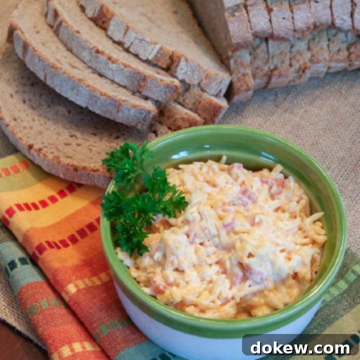 Homemade Pimento Cheese Homemade Pimento Cheese in a green and white bowl, garnished with a sprig of parsley. There is an unpackaged loaf of sliced bread at the top of the photo.
