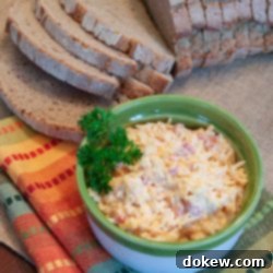 Southern Pimento Cheese Perfection 2 Homemade Pimento Cheese in a green and white bowl, garnished with a sprig of parsley. There is an unpackaged loaf of sliced bread at the top of the photo.