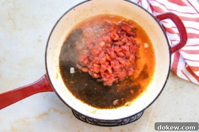Savory Swiss Steak Worcestershire sauce and diced tomatoes combined in a red and white skillet, ready to simmer.
