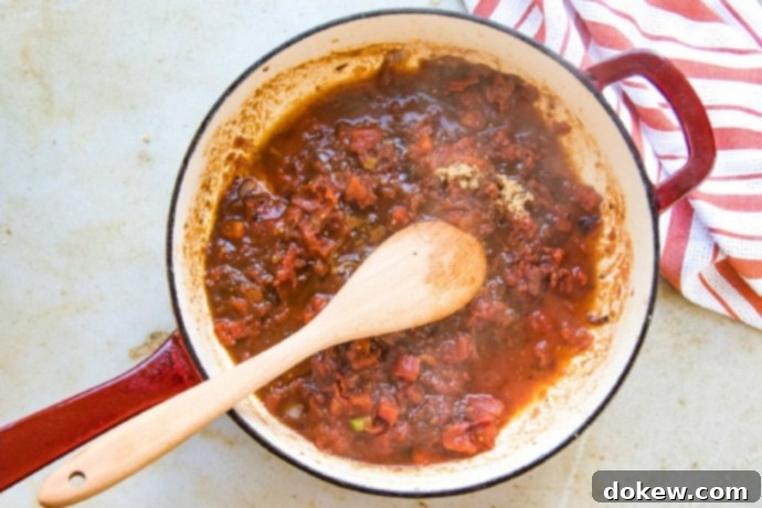 Savory Swiss Steak Cooked Worcestershire sauce and tomato mixture simmering in a red and white skillet, showing deglazing in progress.