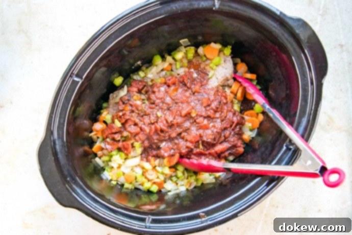 Savory Swiss Steak Chopped onion, carrots, and celery topped with Worcestershire sauce and tomato mixture in a slow cooker, ready for cooking.