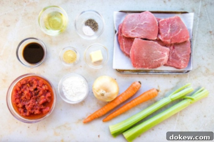 Savory Swiss Steak Photo is ingredients in separate clear glass bowls: diced tomatoes, Worcestershire sauce, oil, salt and pepper, dry mustard, flour, butter. There are 6 beef steaks on a metal pan. An onion, two carrots, and two stalks of celery are on the counter next to the pan.