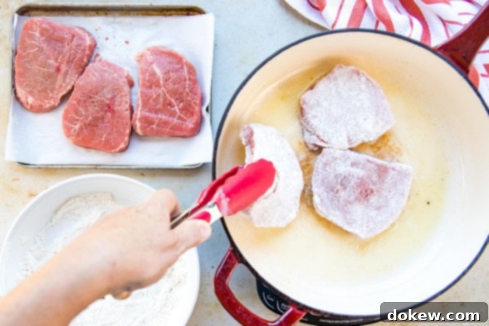 Savory Swiss Steak Three floured beef steaks browning in a red and white skillet. Beside are more raw, floured steaks and seasoning.