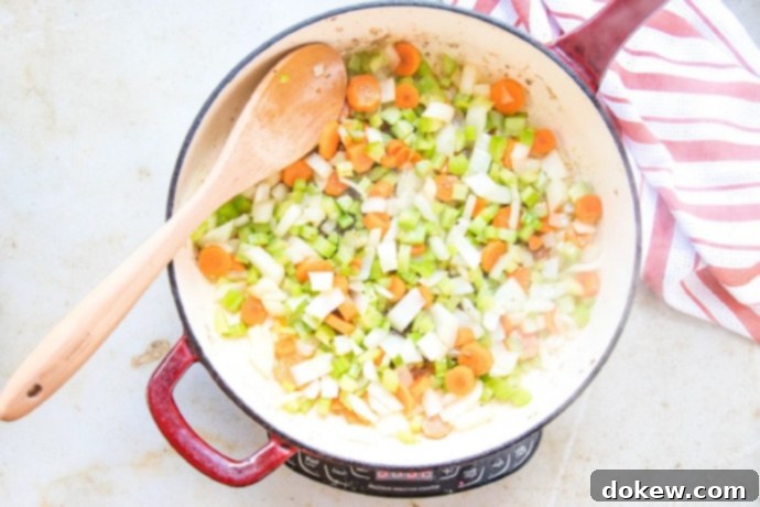 Savory Swiss Steak Chopped onion, carrots, and celery sautéing in a red and white skillet with a wooden spoon.