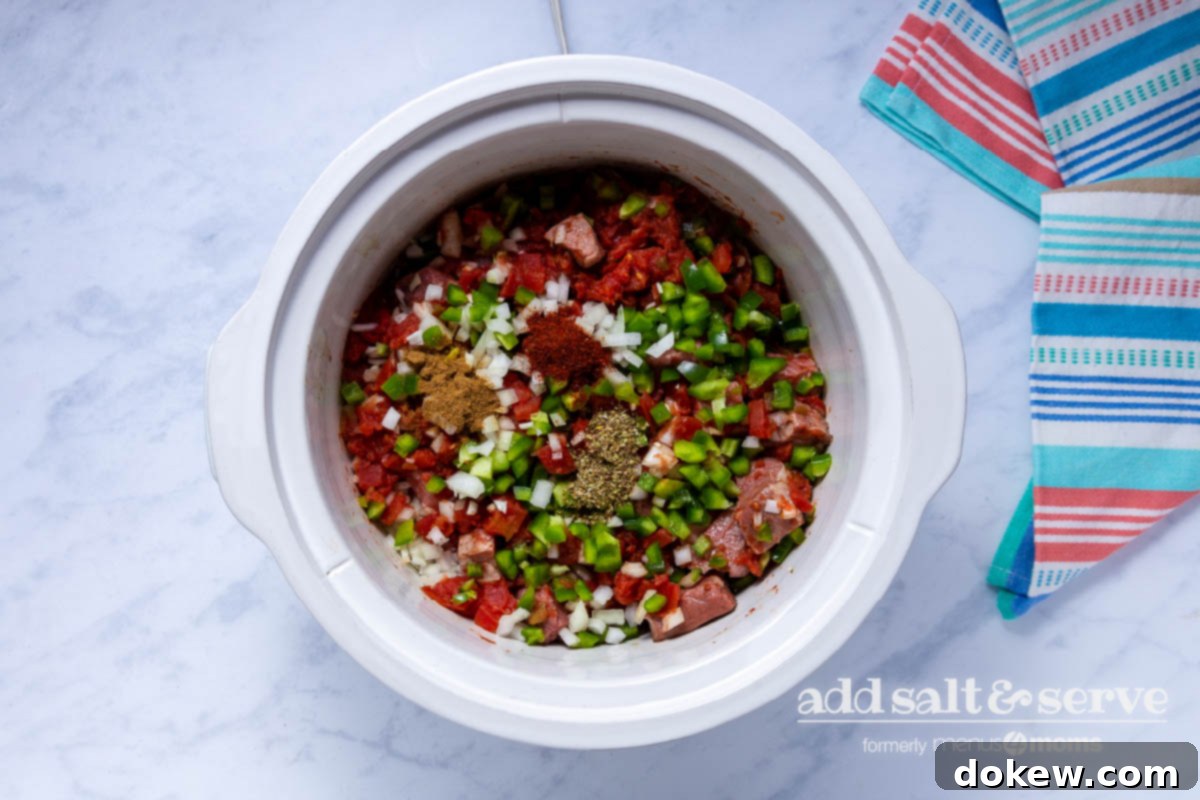 Slow Cooker Tender Beef Guisada 6 Overhead view of meat, vegetables, and spices for Carne Guisada in a crock pot.