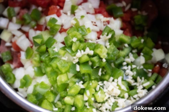 Layering Ingredients for Instant Pot Carne Guisada The inner pot of an Instant Pot, showing layers of raw beef stew meat at the bottom, topped with vibrant diced tomatoes and green chilies, then freshly chopped onion, green bell pepper, and minced garlic, ready for pressure cooking. This image highlights the 'dump-and-go' assembly for the stew.