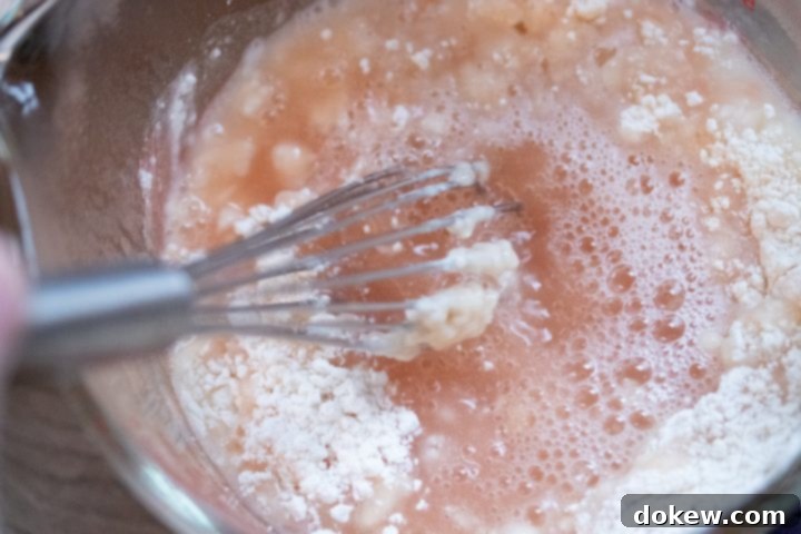 Preparing the Flour Slurry for Carne Guisada Gravy Close-up of a glass measuring cup where 3 tablespoons of flour are being whisked into a mixture of reserved tomato juices and water, creating a smooth, light-colored slurry. This is for thickening the Carne Guisada.