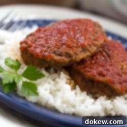 Easy Baked Swiss Burgers 3 Two Baked Swiss Hamburgers on a bed of rice on a plate, showcasing the rich tomato-based gravy.