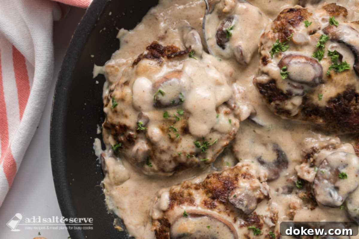 Rich Salisbury Steak in a Velvety Mushroom Sauce 6 Several Salisbury Steak patties in mushroom cream sauce in a black pan.