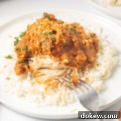 Weeknight Thai Peanut Chicken Magic 9 Plated slow cooker Thai Peanut Chicken over rice garnished with chopped peanuts and cilantro with a fork cutting into the chicken showing white breast meat.