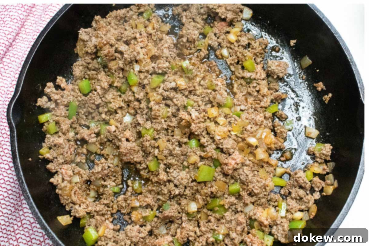 Cornbread Burger Casserole 3 Cooked ground beef, diced onions and bell peppers are seasoned with chili powder and salt, sautéing until tender in a sturdy cast iron skillet, ready for the next step of the casserole.