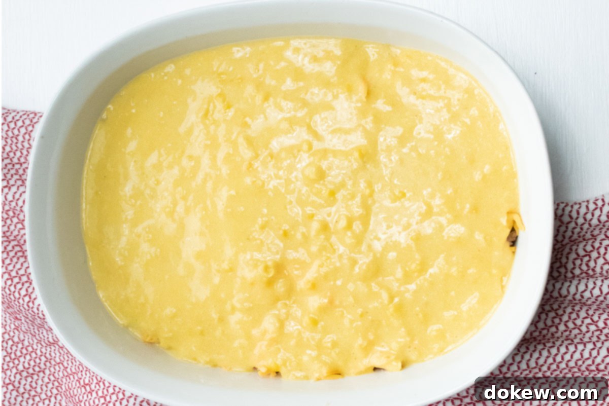 Cornbread Burger Casserole 5 A white casserole dish is now topped with a smooth, light yellow layer of cornbread batter, ready to be baked into a golden, delicious crust.