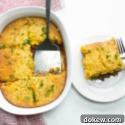Cornbread Burger Casserole 6 A hearty slice of Cornbread Burger Bake is served on a plate, alongside the full casserole dish. This comforting meal features seasoned ground beef and vegetables under a golden cornbread topping.