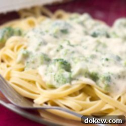Creamy Broccoli Alfredo with Fettuccine 3 Afredo sauce with broccoli over fettuccine on a clear glass plate with a fork