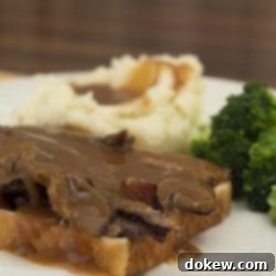 Slow-Roasted Beef Sandwich 3 Photo of a slice of white bread with sliced roast beef and gravy, with mashed potatoes and gravy and cooked brocoli florets on a white plate