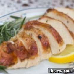Lemon-Kissed Rosemary Chicken 2 slices of roasted chicken garnished with fresh rosemary and lemon slices on a white plate