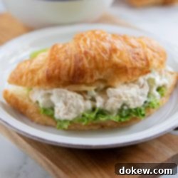 Flaky Croissant Chicken Salad Creations 3 White plate with chicken salad on a bed of lettuce on a croissant, sitting on a brown table with a white bowl in the background