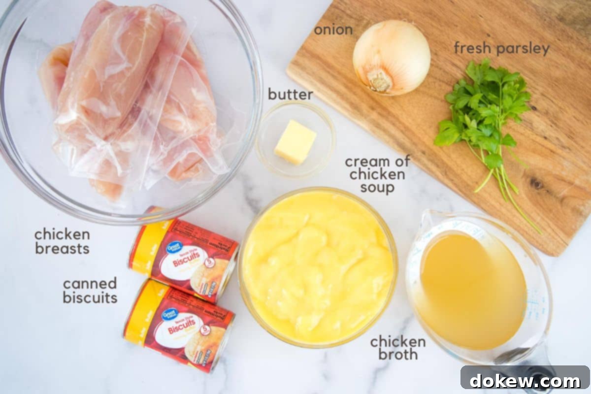 Easy Crockpot Chicken & Dumplings Individually wrapped chicken breasts in a clear glass bowl, two tablespoon butter in a small clear glass bowl, two cans of refrigerated biscuits, cream of chicken soup in a clear glass bowl, chicken broth in a clear measuring cup, and one onion and some sprigs of parsley on a cutting board.