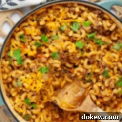 One Pot Taco Macaroni in 30 Minutes 12 Skillet of cheesy elbow macaroni and ground beef in a seasoned tomato sauce garnished with cilantro, ready to be served.