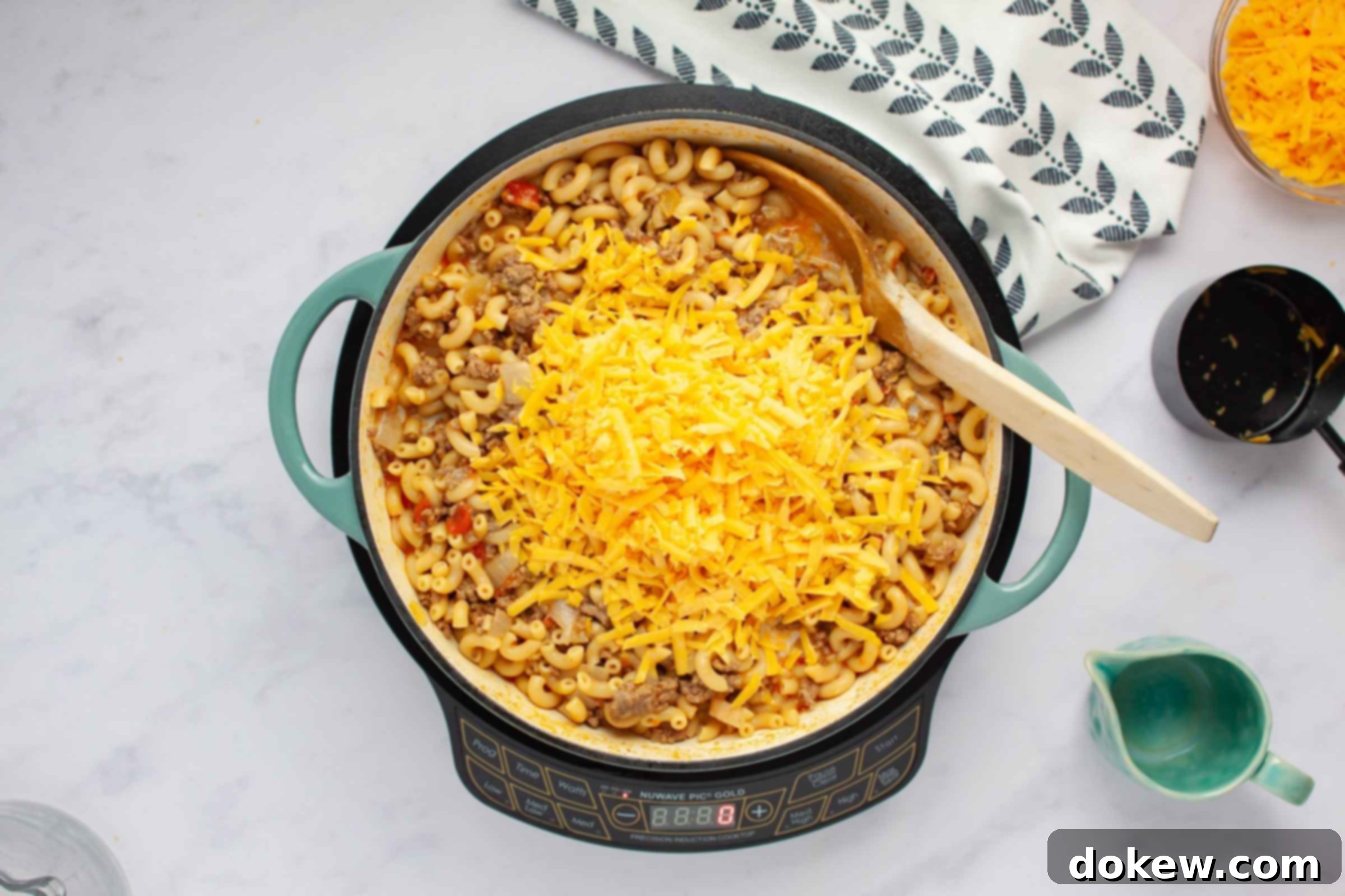One Pot Taco Macaroni in 30 Minutes 10 Skillet with ground beef and elbow macaroni in a seasoned tomato sauce with shredded cheddar cheese added but not stirred in.