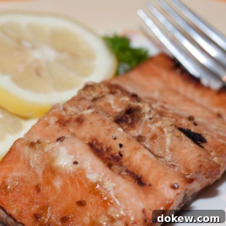Easy Baked Salmon Teriyaki Pieces of cooked salmon on a white plate with a fork, garnished with two lemon slices and parsley