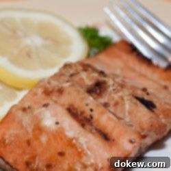 Simple Teriyaki Salmon Bake 2 Pieces of cooked salmon on a white plate with a fork, garnished with two lemon slices and parsley