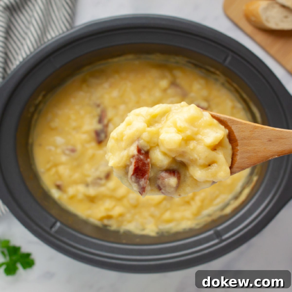 Hearty Cheesy Kielbasa Potato Slow Cooker Soup 5 Close-up of a spoonful of potato soup with kielbasa pieces on a wooden spoon held over a crockpot of the soup, showing the rich, cheesy texture.