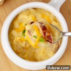 Hearty Cheesy Kielbasa Potato Slow Cooker Soup 7 Closeup of a spoonful of potato soup with kielbasa garnished with shredded cheddar cheese and sliced green onion held above a crock of the soup, emphasizing its comforting appeal.