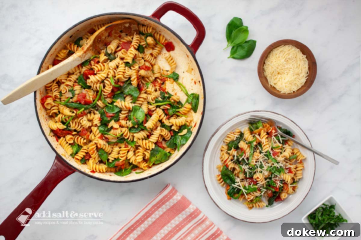 Quick and Easy One-Pot Tomato Spinach Pasta 2 Plate of tomato Spinach Pasta garnished with Parmesan cheese and fresh basil strips on a counter beside the pan of the full dish.