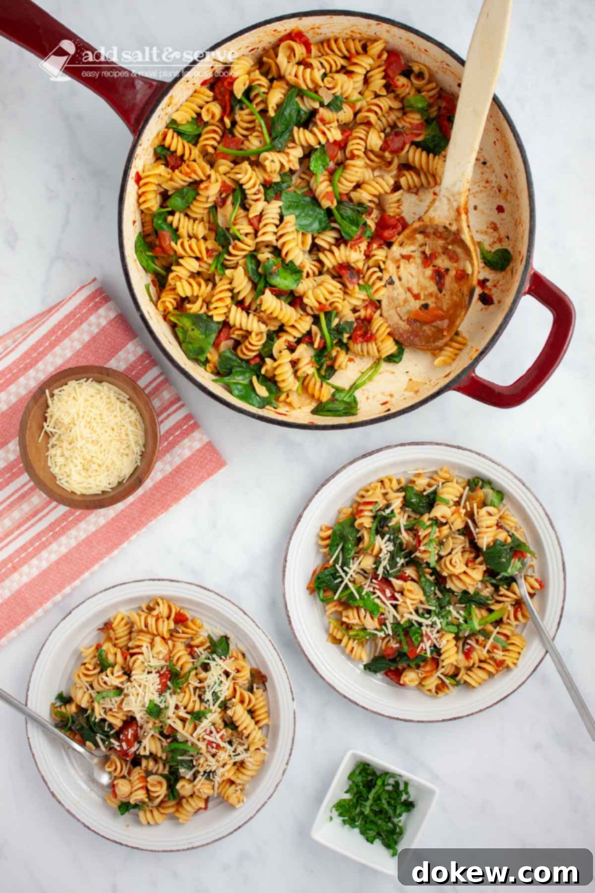 Quick and Easy One-Pot Tomato Spinach Pasta 6 Two plates of tomato Spinach Pasta garnished with Parmesan cheese and fresh basil strips on a counter beside the pan of the full dish and small bowls of parmesan cheese and fresh basil strips.
